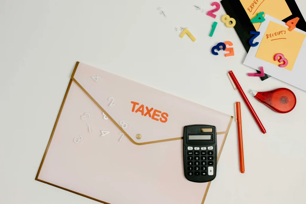 Flat lay view of a tax document folder labeled TAXES next to a calculator, receipts, and stationery on a white desk.