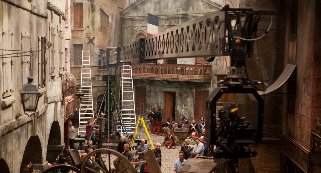 Professional camera crane and crew filming on an elaborate period street sound stage at a UK movie studio.